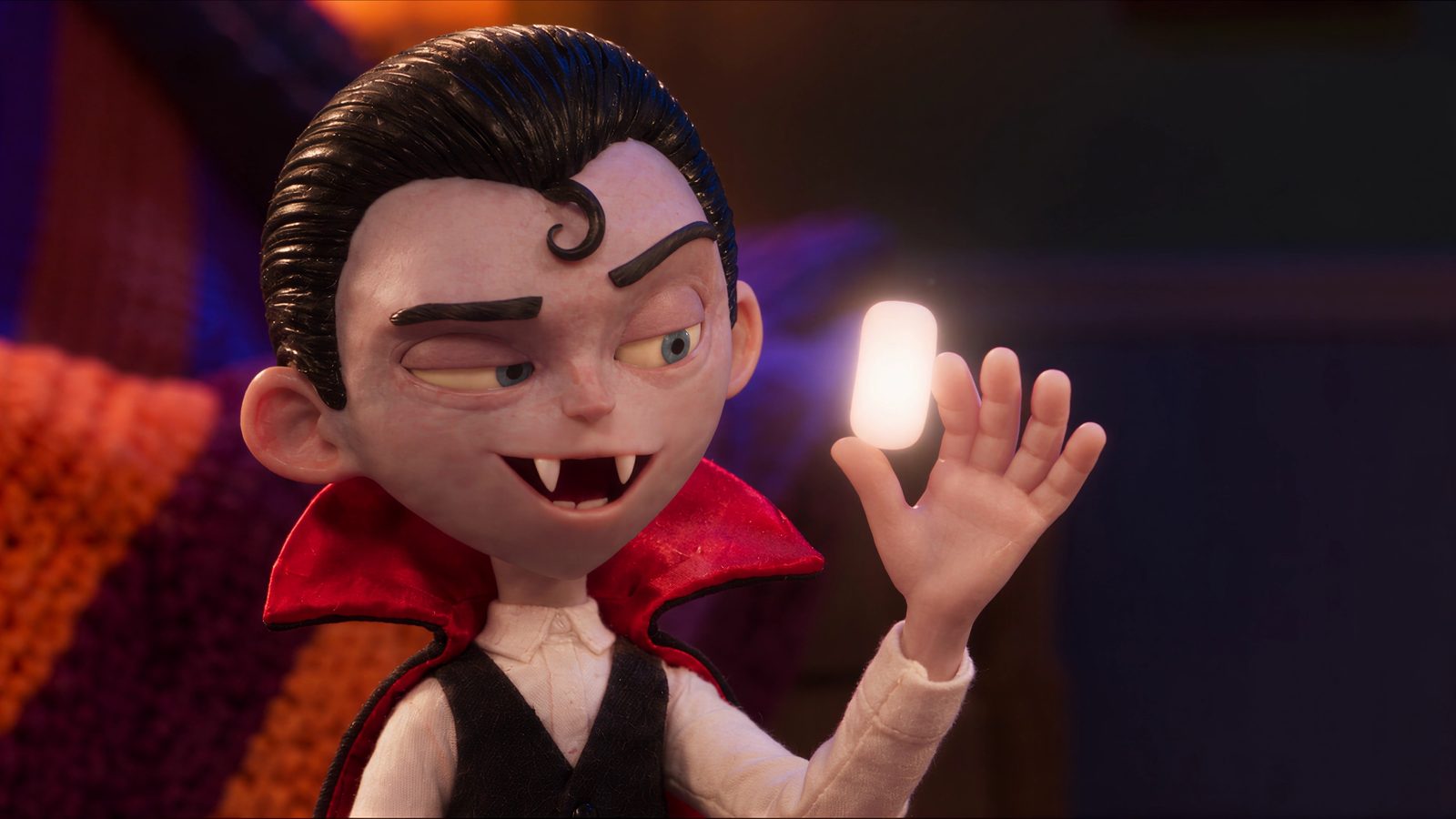 A boy in a vampire cape grins and holds up a softly glowing candy