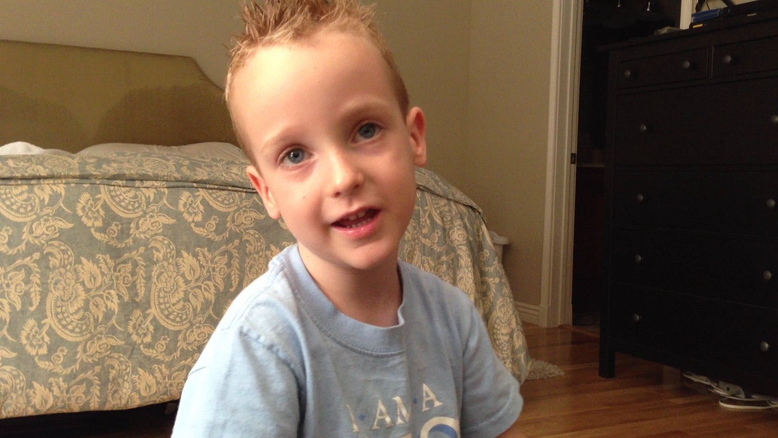 A four-year-old boy on his bedroom floor, mid-pitch, looking into the camera